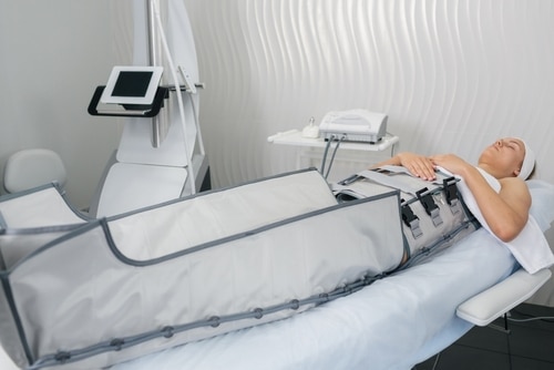 Séance de pressothérapie pour drainage lymphatique. Une femme est allongée, recouverte d'un vêtement de compression sur les jambes et le ventre.